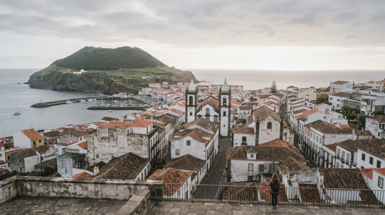 Whitewashed buildings and the marina front of Angra do Heroísmo seen from the bay, with the green slope of Monte Brasil behind
