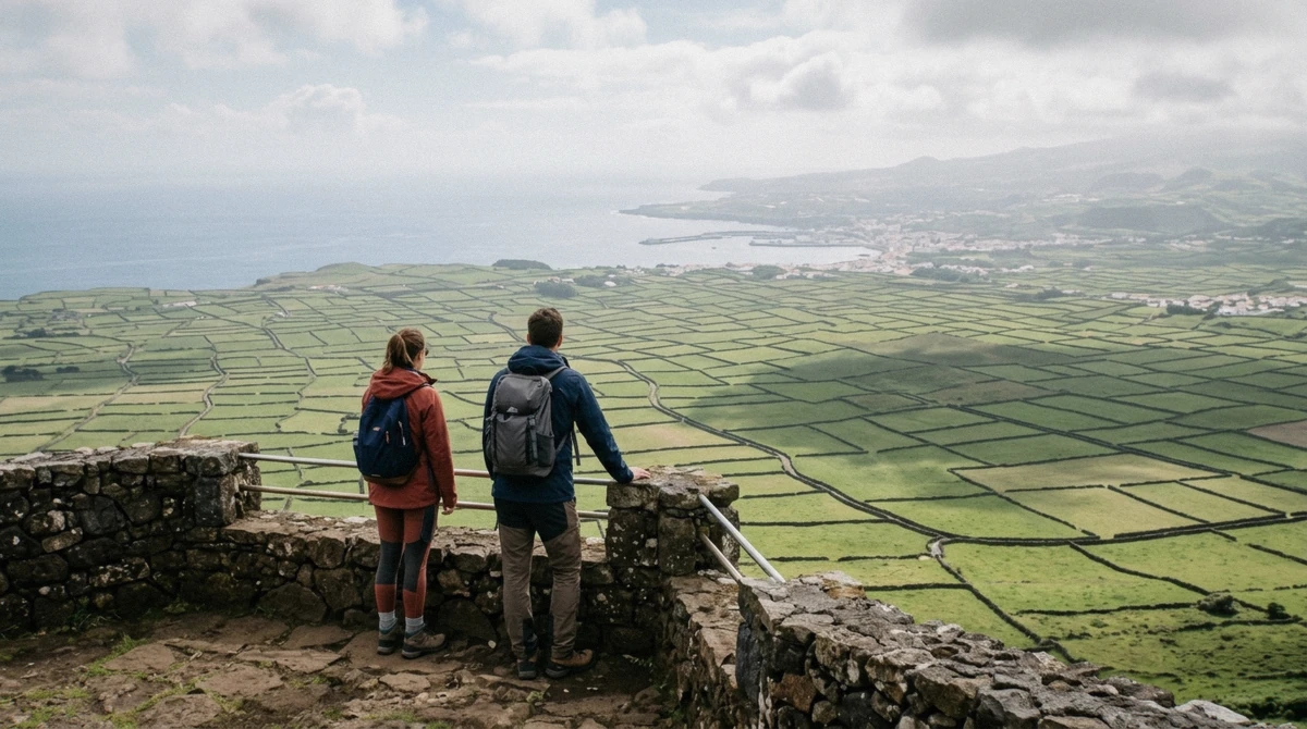 A traveller seen from behind on a viewpoint walkway above the patchwork fields of Terceira with the Atlantic beyond