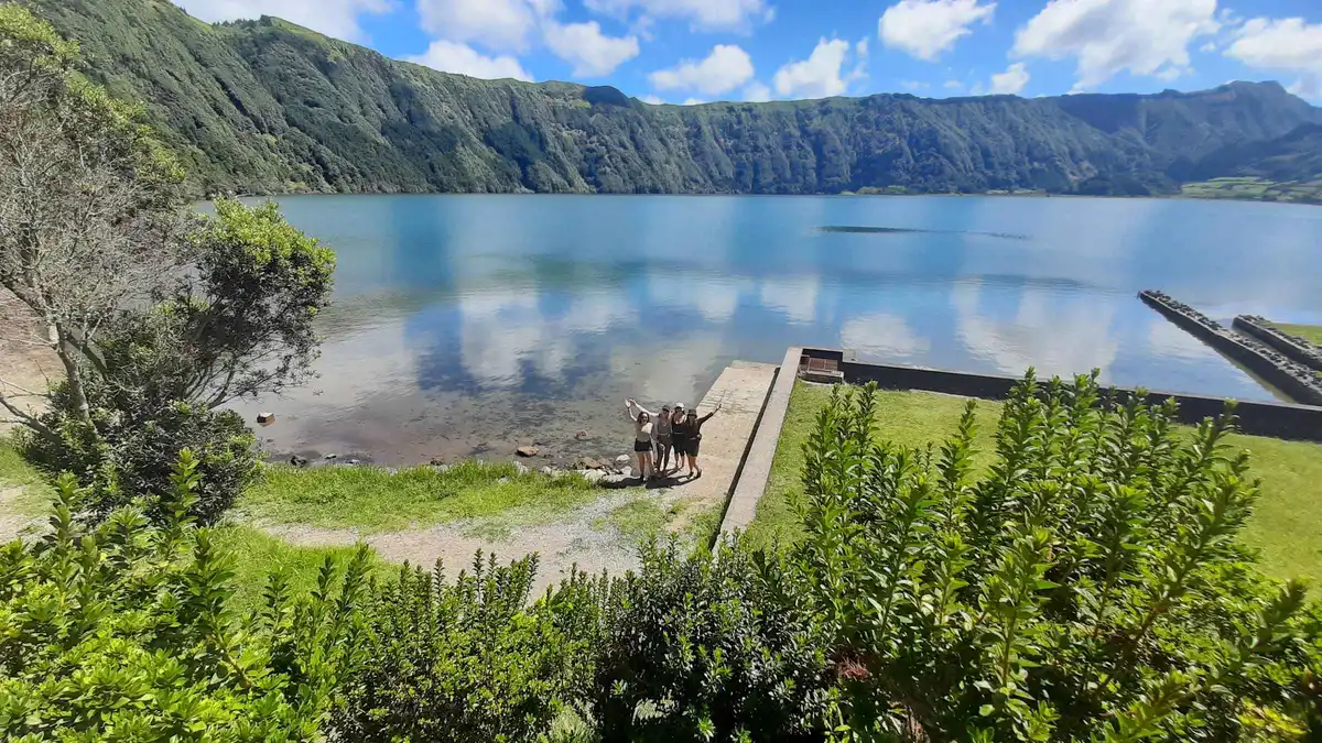 The still waters of the Sete Cidades crater lake seen from the shore, with cattle grazing on the bank