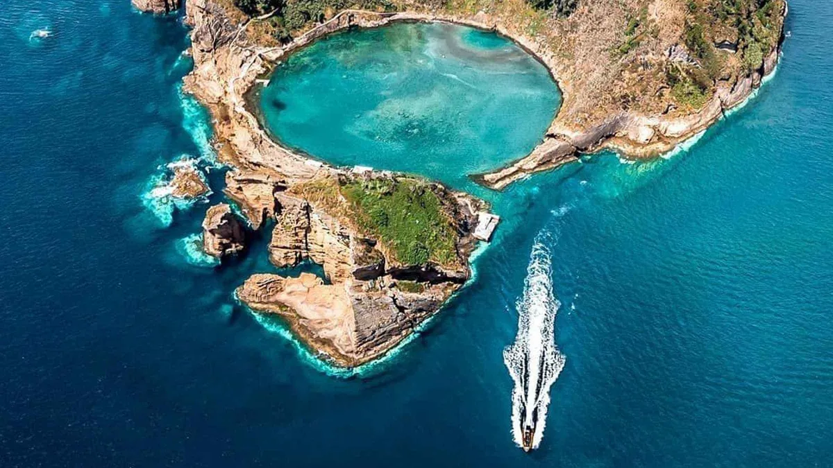 An aerial view of the blue lagoon inside the crater of the Vila Franca do Campo islet, with a boat wake trailing past