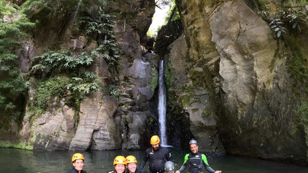 A canyoning group in wetsuits and helmets below a ribbon waterfall in a narrow Salto do Cabrito canyon on Sao Miguel, Azores