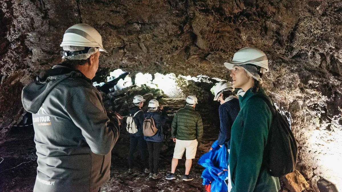 Helmeted visitors inside the vaulted chamber of the Algar do Carvao lava tube on a guided tour