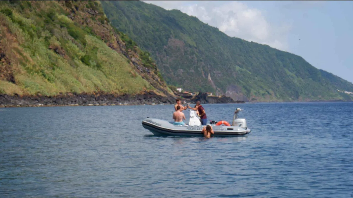 A small rigid boat floating below the steep green cliffs of Sao Jorge on a full-day island tour