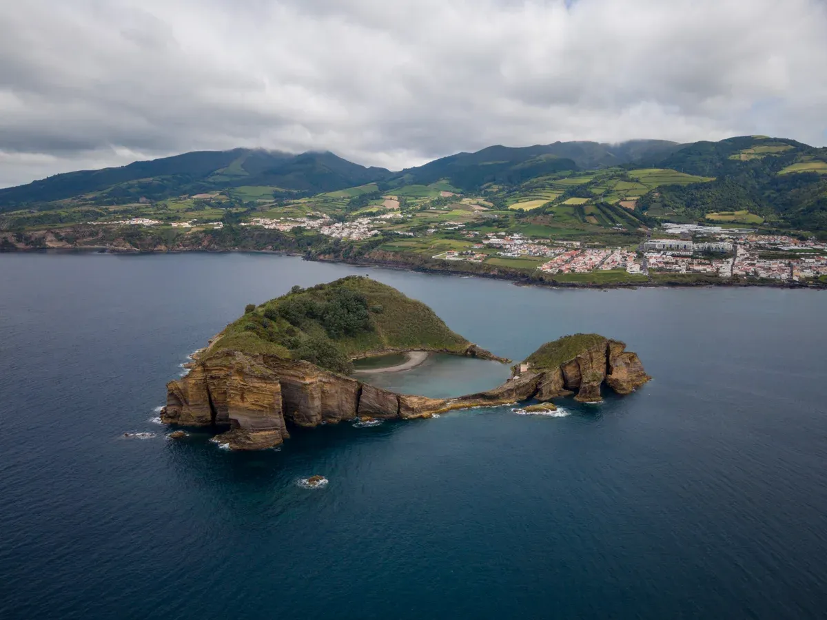 The circular crater islet of Vila Franca do Campo seen from above, its interior lagoon visible, with the town spread along the coast behind